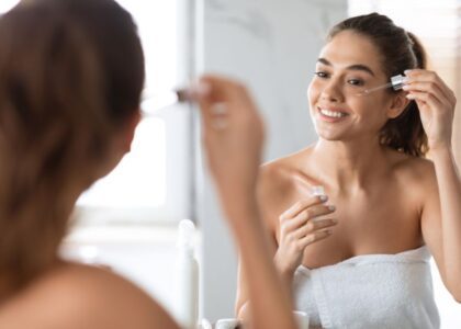 Woman with glowing skin applying a night serum in a relaxing bedroom setting.