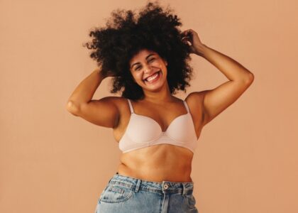 Smiling woman with curly hair wearing a bra and jeans, embracing body positivity.