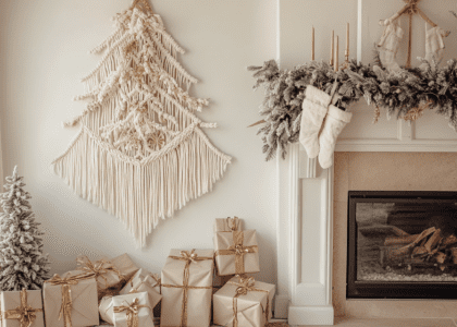 Stylish macramé Christmas tree wall hanging in neutral colors with gold accents, adorned in beige and white tones, positioned next to an elegant fireplace with wrapped gifts underneath, creating a cozy holiday atmosphere.