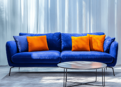 "Elegant living room featuring a European-style blue fabric sofa, silver metal coffee table, and orange pillow, showcasing luxurious design with soft lighting and cinematic textures."