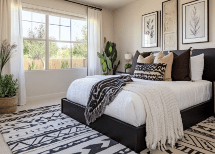 Modern farmhouse-inspired bedroom featuring black and white accents, a neutral color palette, cozy textures, plush pillows, and a blanket on a large bed positioned in front of a window, complemented by wall art, planters, geometric patterns on the rug, and warm natural light creating an inviting atmosphere.