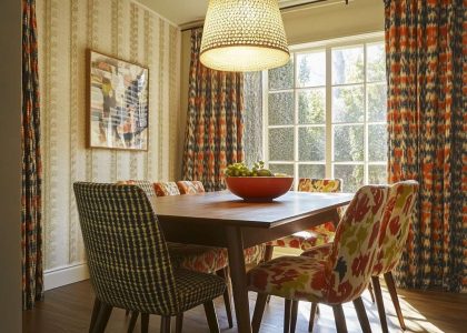 1970s dining room with a sturdy wooden table and mismatched colorful chairs, retro pendant light, patterned curtains, and textured wallpaper creating a cozy atmosphere for family gatherings.