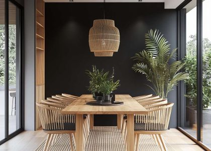 Modern dining room with a black accent wall, light wood dining table, minimalist chairs, woven placemats, and fresh greenery in vases, illuminated by natural light from large windows, creating a cozy and elegant atmosphere.