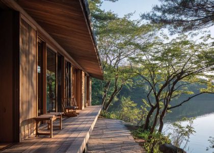 Serene Japanese lakehouse with sliding wooden screens, soft sunlight filtering through, natural wood exterior blending with muted earth tones and granite, tranquil setting by calm waters, shadows elongating in the evening light.