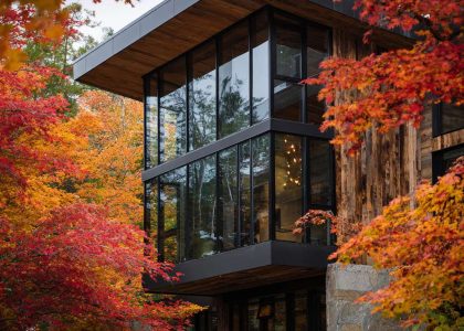 Alpine modern lakehouse facade surrounded by autumn foliage featuring dark timber and glass, large panoramic windows, and a blend of contemporary design with nature.