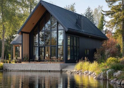Sleek modern barn lakehouse with classic gabled roof and vertical black barn siding, featuring tall windows that showcase stunning lakeside views and a serene atmosphere by the water's edge.