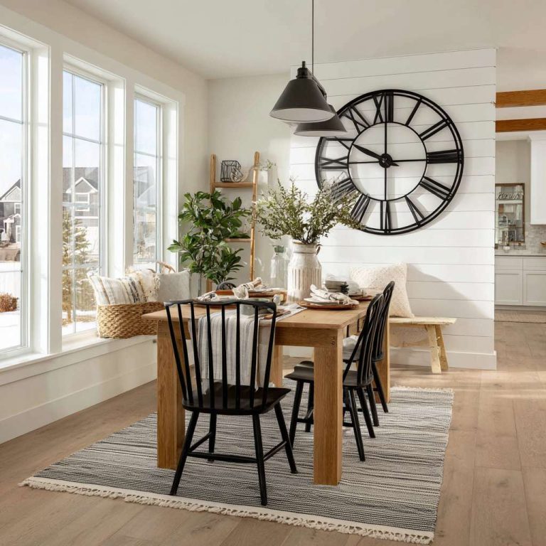 Modern farmhouse dining room with white shiplap accent wall, oversized black metal clock, natural wood accents, and sunlight filtering through large windows, creating an inviting atmosphere for family gatherings.