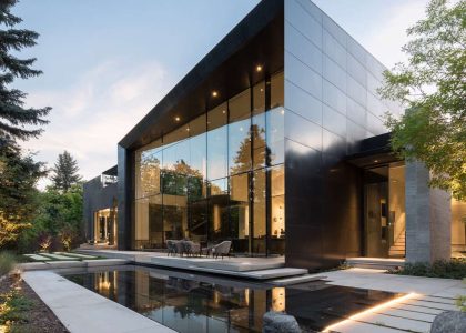 Sleek modern house facade with floor-to-ceiling glass walls, dark metal panels, sharp angles, and minimalist landscape, showcasing sophisticated and serene indoor-outdoor living.